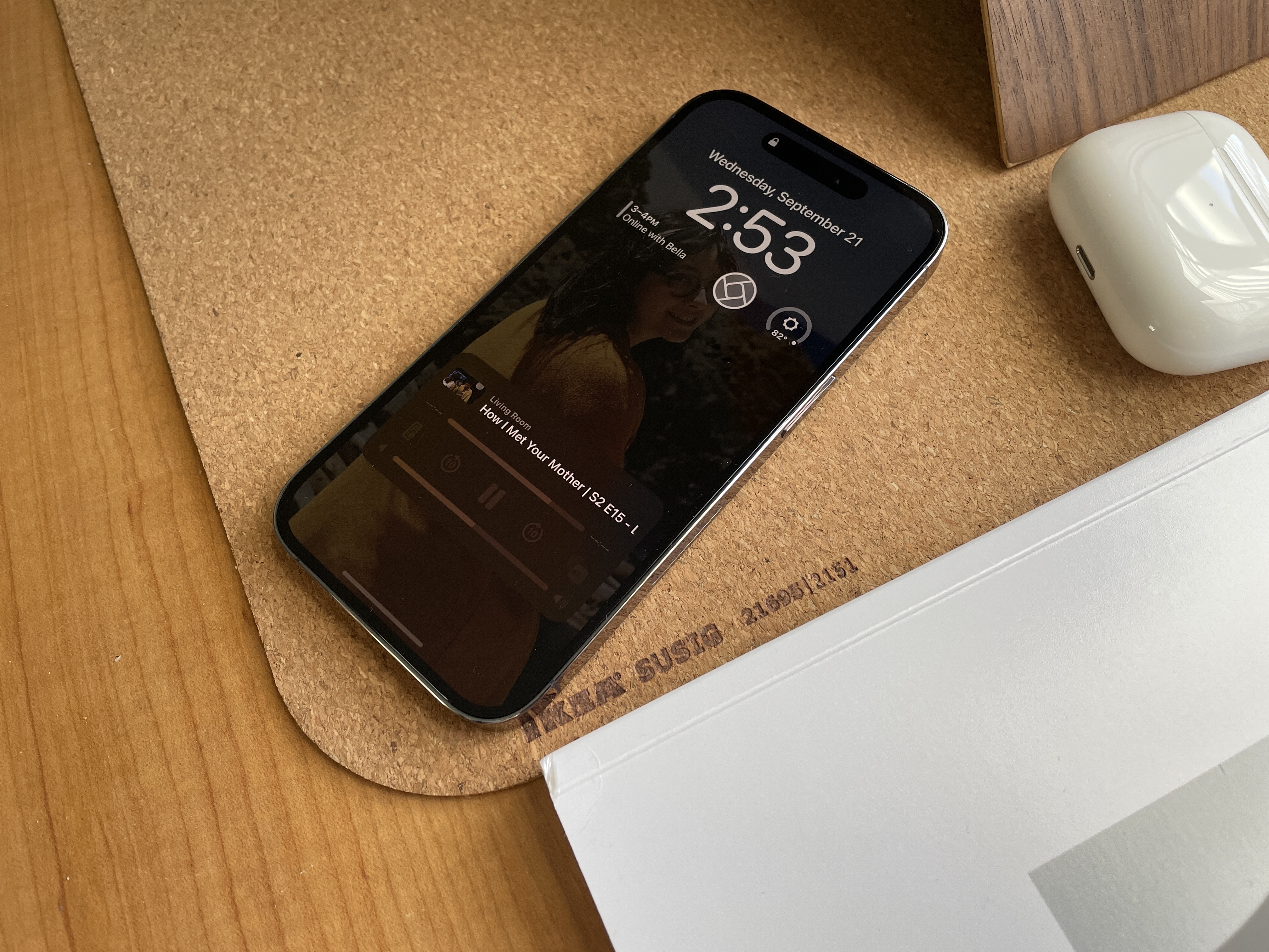 The iPhone 14 on a desk with the always on display showing lock screen widgets and the now playing widget at the bottom.
